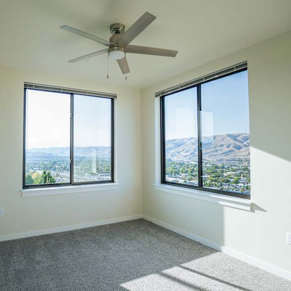 a room with a ceiling fan and two windows overlooking a cityscape.