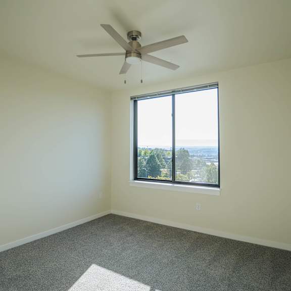 a room with a ceiling fan and a window overlooking a cityscape.