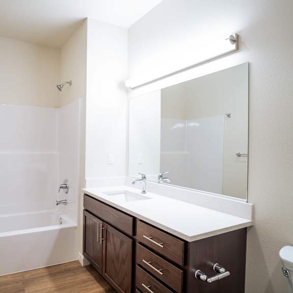 a white bathroom with a brown vanity and a white tub.