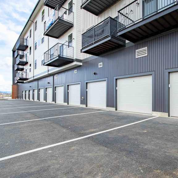 a parking lot in front of a grey building with a balcony on the second floor.
