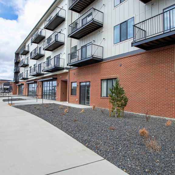 a long building with balconies and a small tree in front.