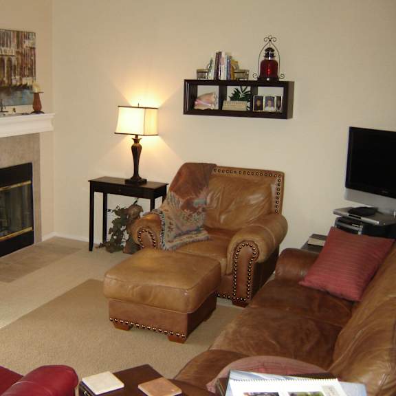 a living room with a fireplace, two chairs, a coffee table, and a painting on the wall.