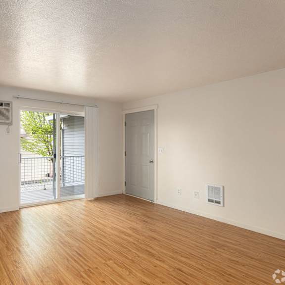 an empty living room with wood floors and a door to a balcony