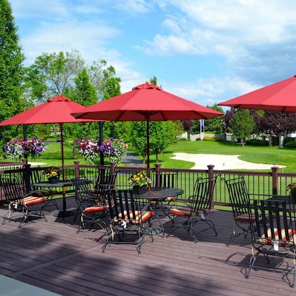 a patio with red umbrellas and chairs overlooking a green lawn.
