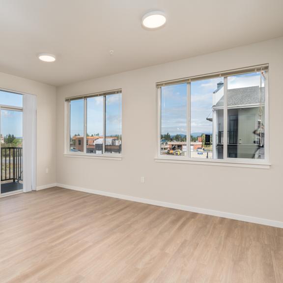 a large empty room with wooden floors and windows overlooking a fenced area.