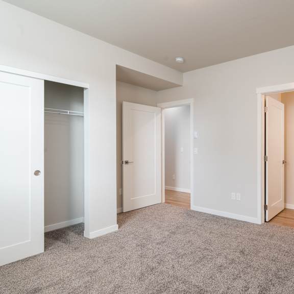 a spacious room with carpeted floor and white walls, with three open doors.