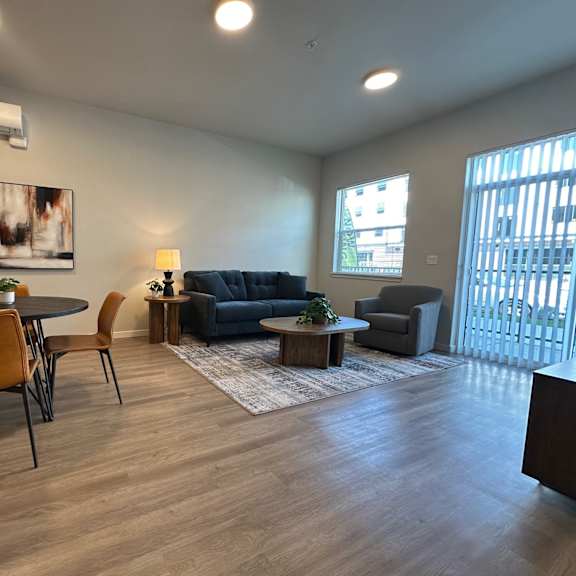a living room with a grey couch, a black cabinet, a round table with four chairs, and a rug.