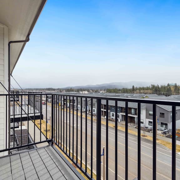 a balcony with a black railing and a view of a parking lot and distant trees.