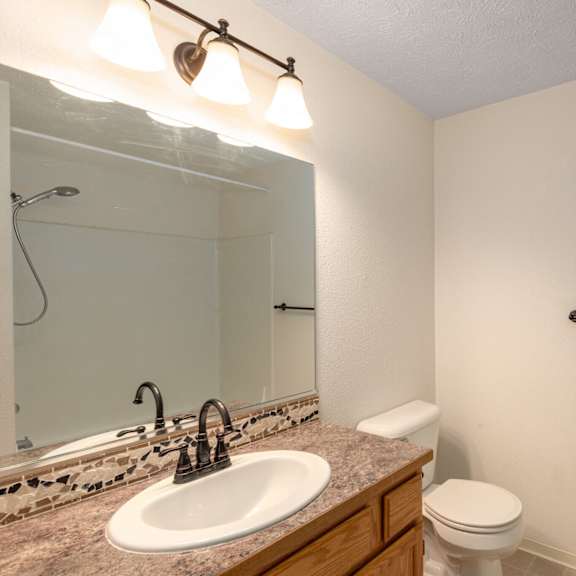 a bathroom with a sink, toilet, mirror, and light fixture.