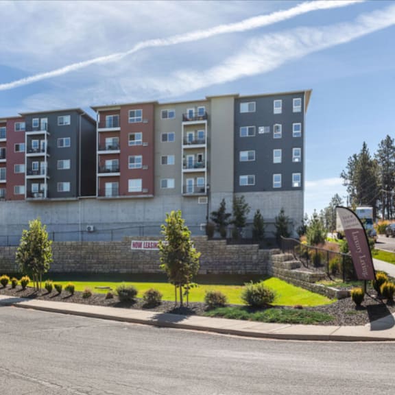 a row of multi-story apartment buildings with trees and shrubs in front.