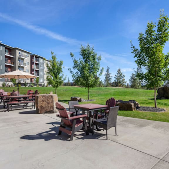 a patio with a table and chairs is surrounded by trees and apartment buildings.