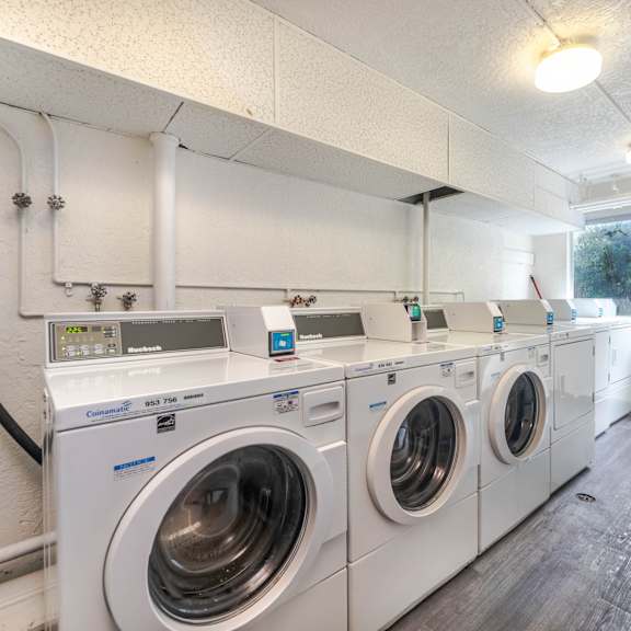 a row of white front load washing machines in a laundry room.