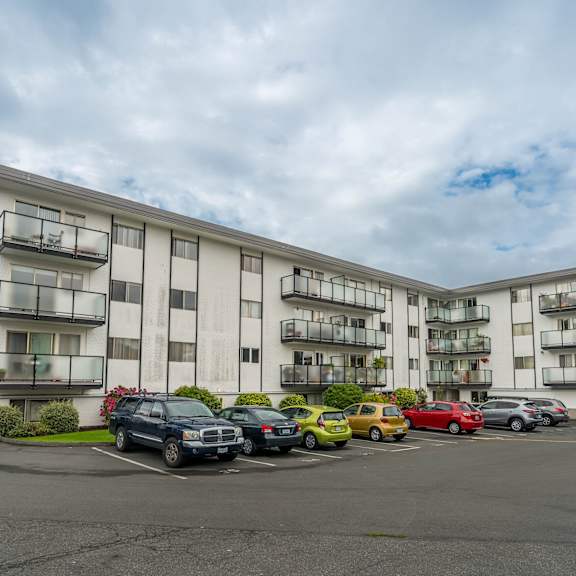 a large white apartment building with cars parked in front.
