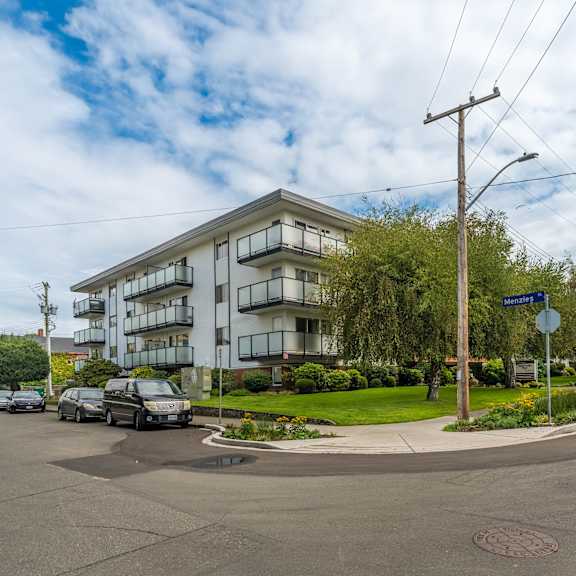 a street view of a residential area with apartment buildings and cars parked on the side of the road.