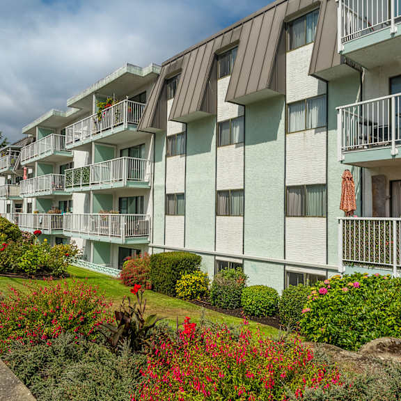 a row of apartment buildings with balconies and flower beds in front.