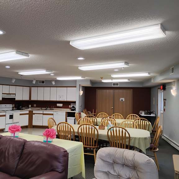 a room with tables and chairs and a kitchen in the background.