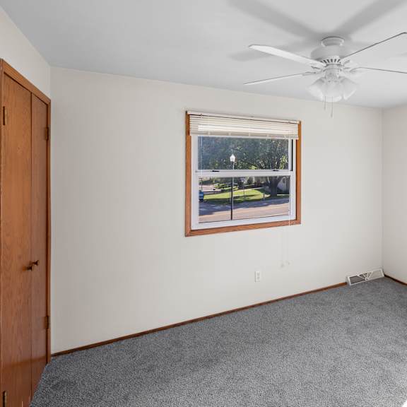 a room with a ceiling fan and two windows.