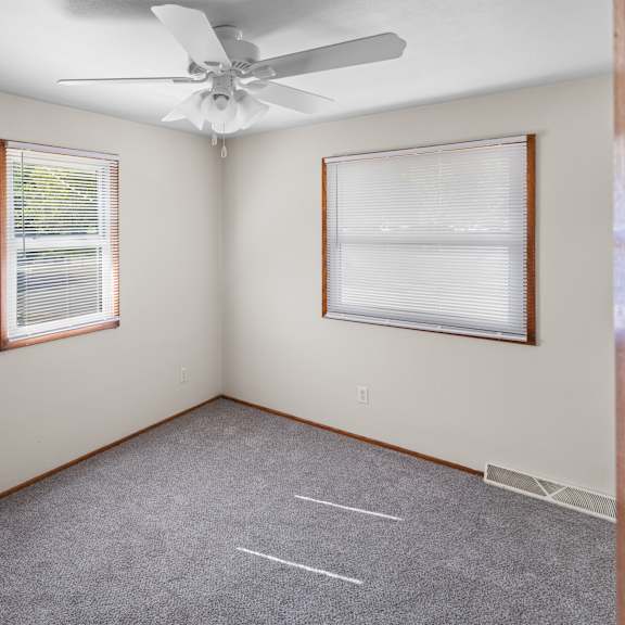 a room with a ceiling fan and two windows.