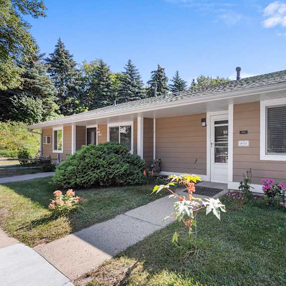 a small house with a brown and white exterior is surrounded by greenery and flowers.