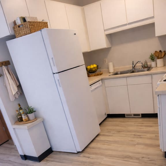 a white refrigerator stands in a kitchen with wooden flooring.