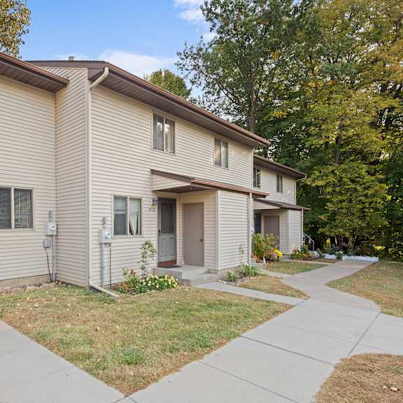 a beige two-story apartment building with a brown roof and a small front yard.