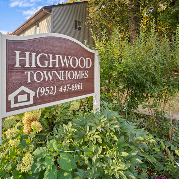 a sign for highwood townhomes stands in front of a building and some trees.