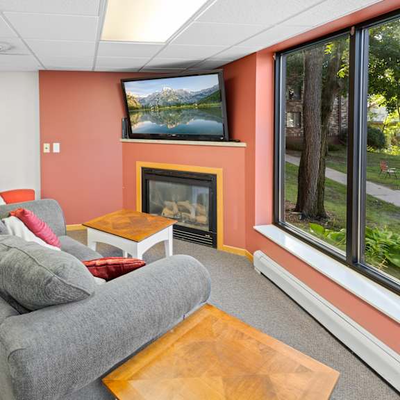 a grey couch with a pillow and a small table in front of a fireplace.