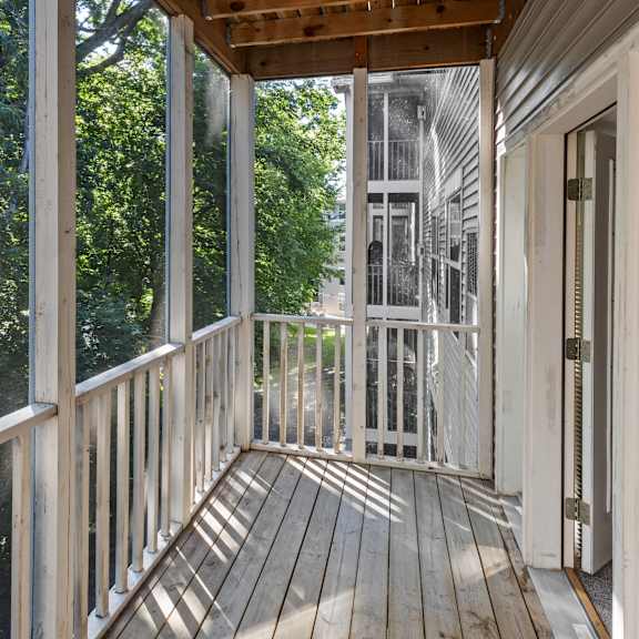a wooden deck with a railing and a view of trees and a building in the background.