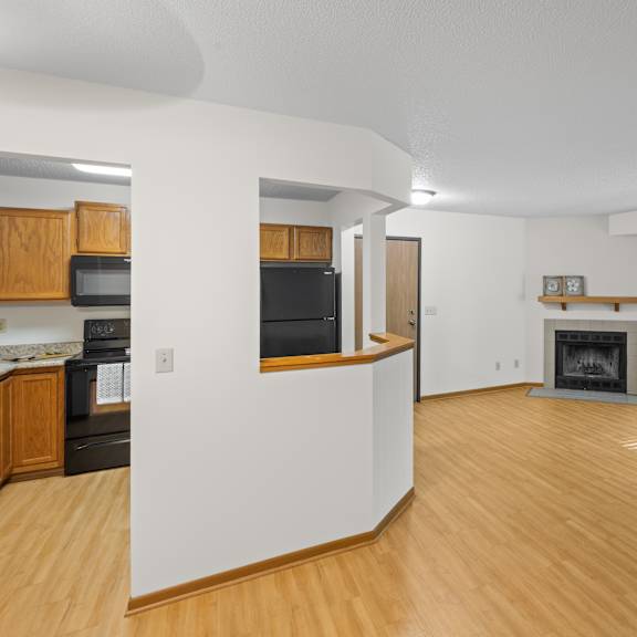 a living room with a fireplace and a kitchen area with wooden cabinets.