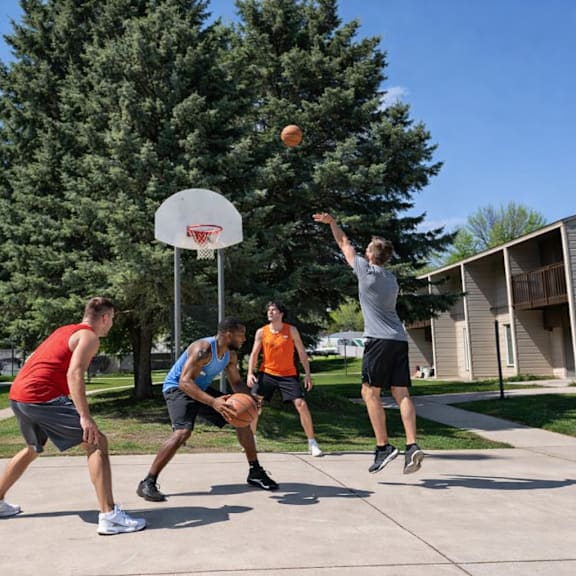 three men playing basketball on a sunny day.