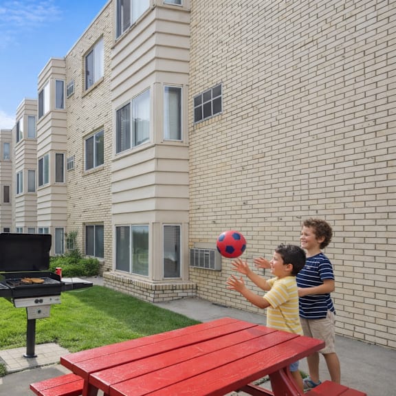 a man and a woman are standing by a grill with two children playing with a ball.