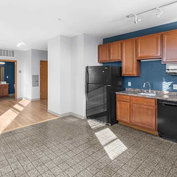 a kitchen area with a black refrigerator and wooden cabinets.