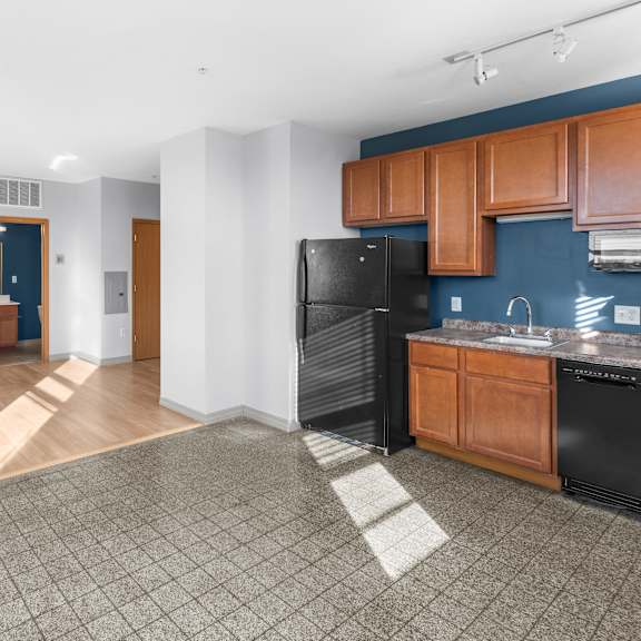 a living room with a kitchen and a black refrigerator