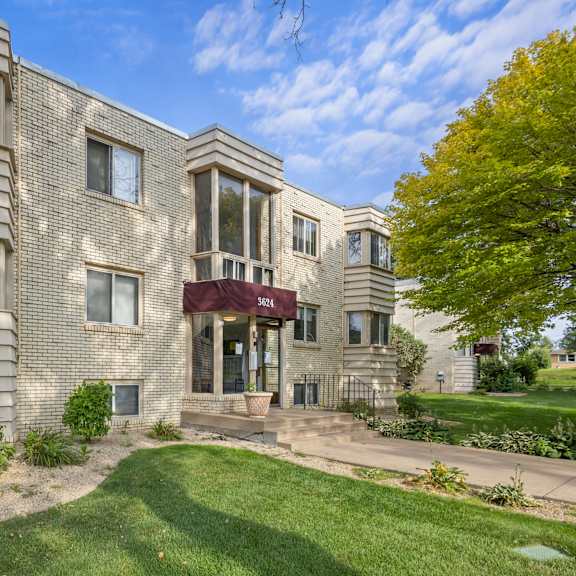 the front of a brick apartment building with green grass and trees