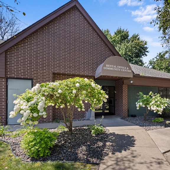 the front of a brick building with a sidewalk and trees