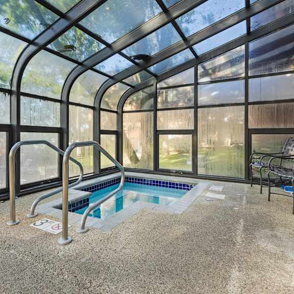 a indoor hot tub in a greenhouse with chairs and a wall of windows