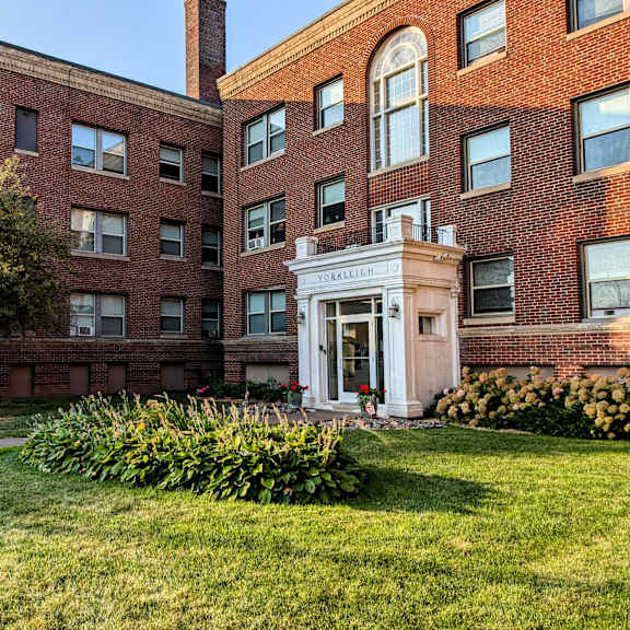 the front of a brick building with a porch and a lawn