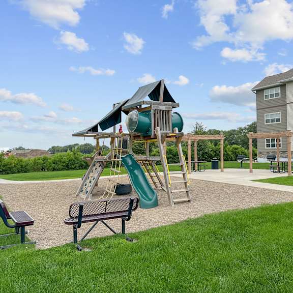a playground with a green slide and a wooden swing set.