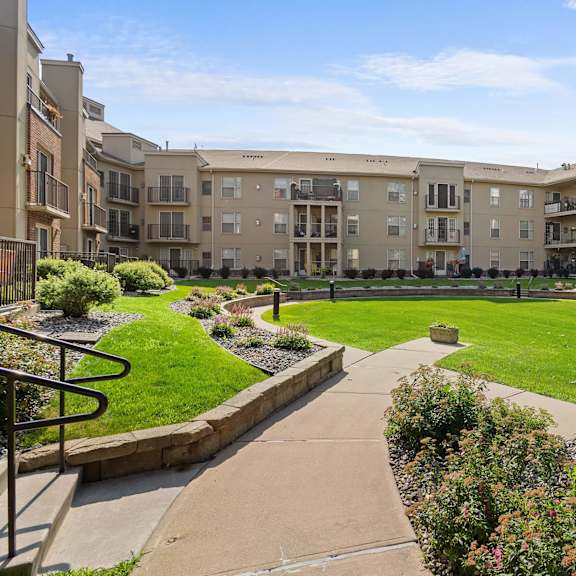 a sunny day at a well-maintained apartment complex with a green lawn and walking paths.