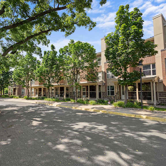 a tree-lined street in front of a brick apartment building.