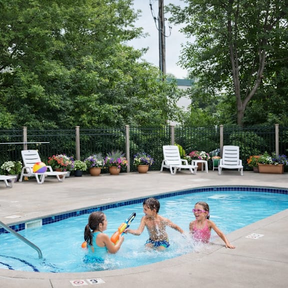 three children playing in a pool surrounded by lounge chairs and greenery.