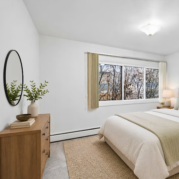 a bedroom with a large bed, a wooden dresser, and a window with a view of trees outside.