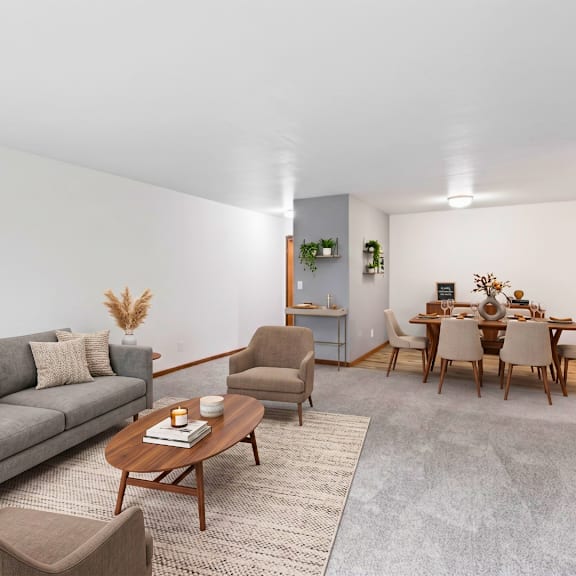 a living room with a grey couch, a wooden coffee table, and a dining table set up.