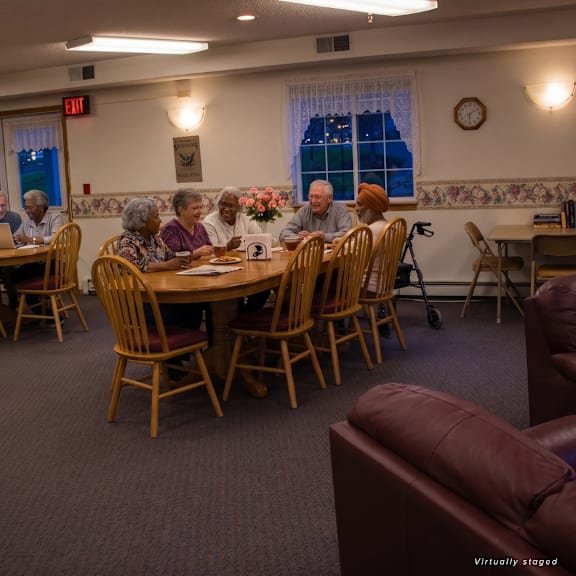 a group of elderly people are sitting around a table in a room with wooden chairs.