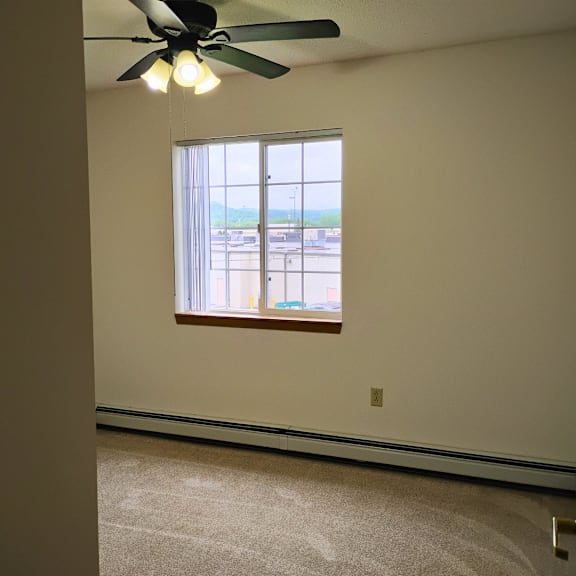 a room with a ceiling fan and a window overlooking a parking lot.