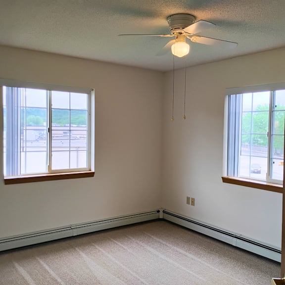 a room with a ceiling fan and two windows.