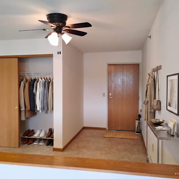 a room with a ceiling fan and a closet with clothes hanging.