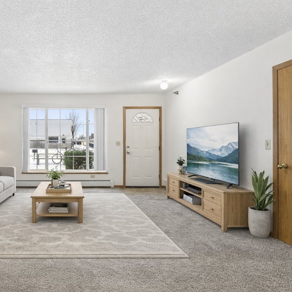 a living room with a grey couch, a wooden side table, a grey rug, a wooden coffee table, a television, a potted plant, and a painting on the wall.
