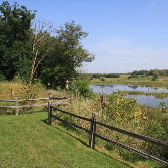 a wooden fence borders a grassy area with a body of water in the distance.