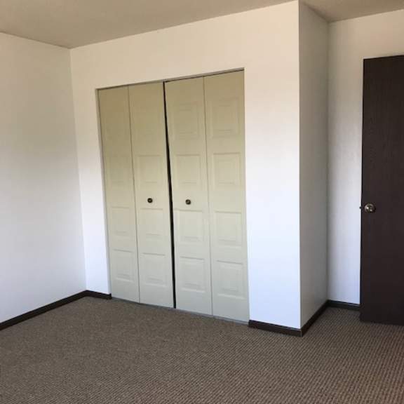 a room with a brown carpet and a white wall with a brown door and a white wardrobe with a mirror.